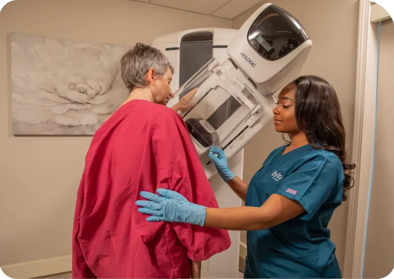 An Aylo nurse is standing next to a patient who is getting her mammogram.